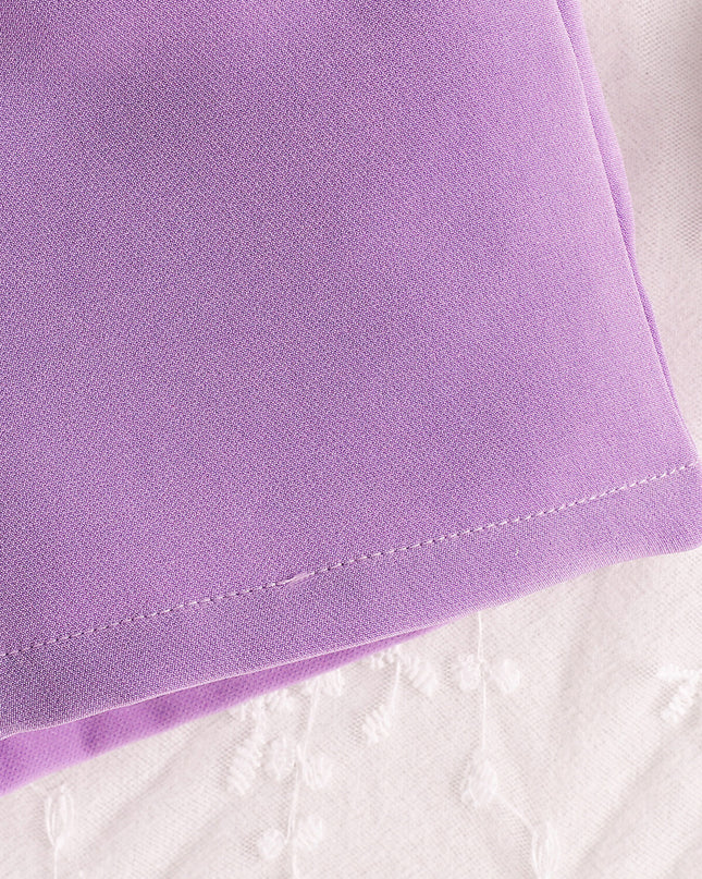 Close-up of lavender fabric with stitching, part of a children's crop top and shorts set.